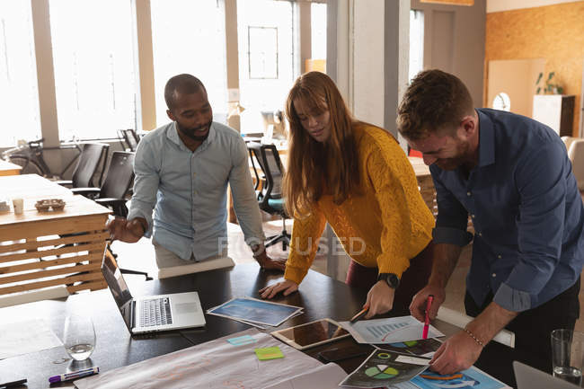 Front view close up of a young African American man and a young Caucasian man and woman standing and leaning over a desk working together on a project in a creative office — Stock Photo