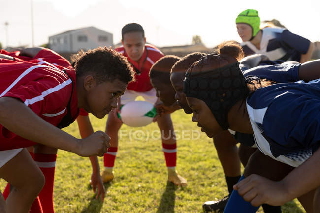 Vista lateral de dos equipos opuestos de jóvenes jugadoras de rugby multiétnicas adultas esperando a que la pelota sea lanzada ante un scrum durante un partido de rugby - foto de stock