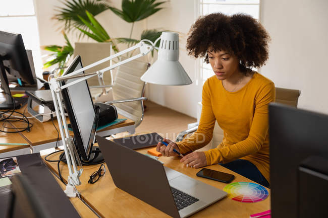 Front view of a young mixed race woman sitting at a desk using a laptop computer at a creative office — Stock Photo