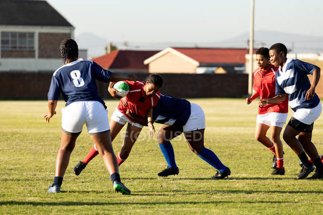 Vista frontal de um grupo de jovens jogadoras de rugby adultas multi-étnicas durante uma partida de rugby com dois jogadores bloqueados em um tackle — Fotografia de Stock