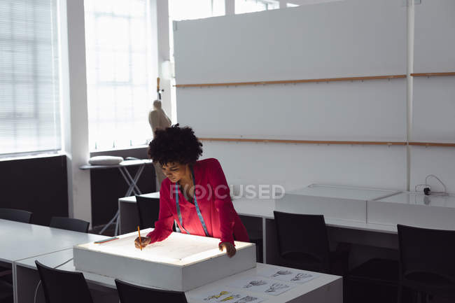 Front view of a young mixed race female fashion student working on a design drawing on a lightbox in a studio at fashion college — Stock Photo
