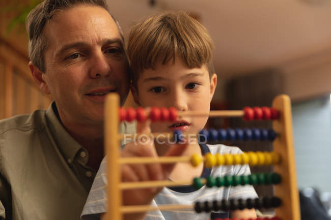 Visão frontal close-up de um homem caucasiano de meia-idade ajudando seu filho pré-adolescente a usar o ábaco — Fotografia de Stock