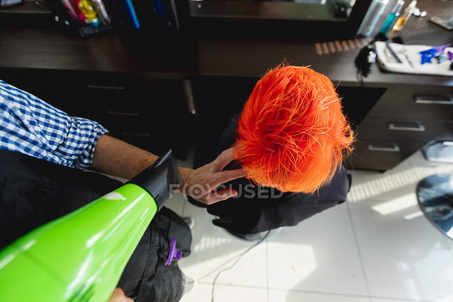 Overhead view close up of male hairdresser and a young Caucasian woman having her hair coloured bright red and blow dried in a hair salon — Stock Photo