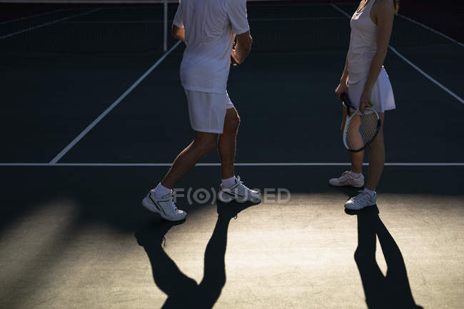 Вид збоку жінки і чоловіка, який грає в теніс в сонячний день, обличчям один до одного і розмовляє — стокове фото