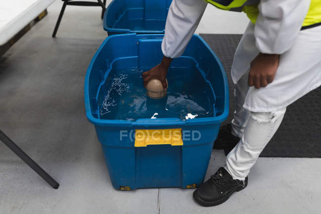 Seitenansicht niedriger Abschnitt eines Fabrikarbeiters, der einen blauen Plastikbehälter mit Flüssigkeit inspiziert — Stockfoto