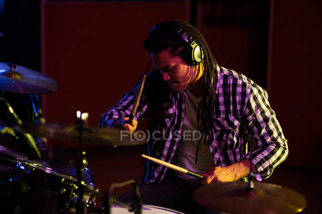 Vista frontal de um jovem baterista misto tocando bateria durante uma sessão em um estúdio de gravação — Fotografia de Stock