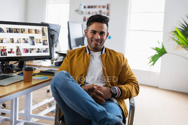 Ritratto di un giovane uomo di razza mista seduto a una scrivania in un ufficio creativo — Foto stock