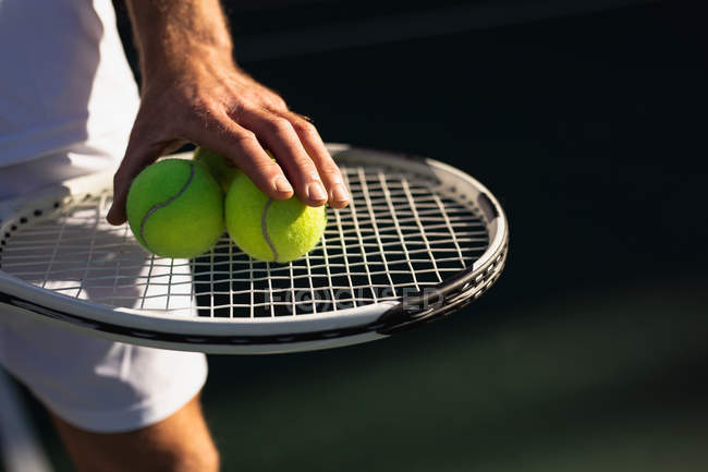 Передний план человека, играющего в теннис в солнечный день, держащего ракетку и мячи — стоковое фото