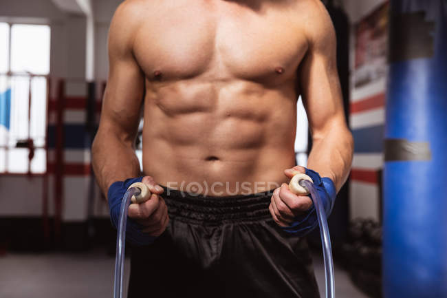 Vista frontal sección media del boxeador masculino sosteniendo una cuerda de salto en un gimnasio de boxeo - foto de stock