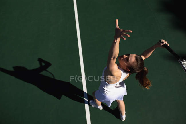 Vista de ângulo alto de uma jovem caucasiana jogando tênis em um dia ensolarado, servindo — Fotografia de Stock