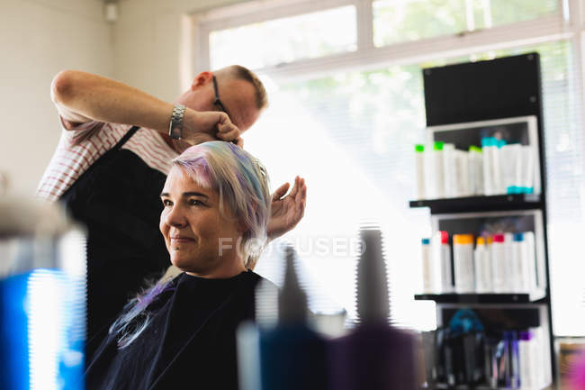 Vista frontal de um cabeleireiro masculino caucasiano de meia idade e uma jovem mulher caucasiana com seu cabelo estilizado em um salão de cabeleireiro — Fotografia de Stock