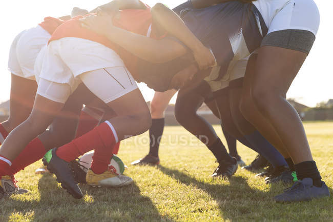 Vista lateral de dos equipos opuestos de jóvenes jugadoras de rugby multiétnicas adultas en un scrum durante un partido de rugby - foto de stock