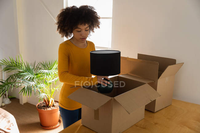 Vista frontal de uma jovem mulher de raça mista desempacotando caixas em um escritório criativo — Fotografia de Stock
