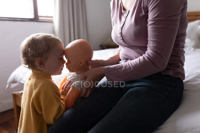 Бічний вид на середину молодої кавказької матері, яка тримає ляльку обличчям до своєї дитини. — стокове фото