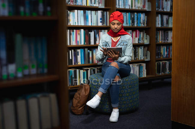 Vorderseite einer jungen asiatischen Studentin mit Turban, die einen Tablet-Computer benutzt und in einer Bibliothek studiert — Stockfoto