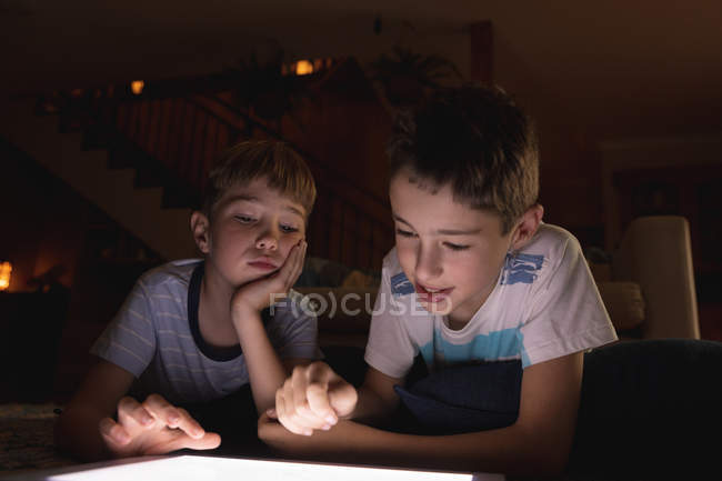 Vista frontal de cerca de dos niños caucásicos preadolescentes usando una tableta en una sala de estar - foto de stock