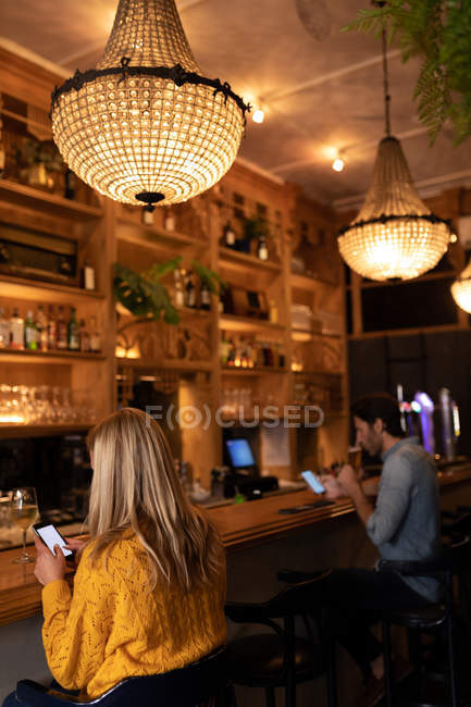 Side view of a young Caucasian man and woman relaxing on holiday in a bar, drinking wine and beer using smartphones — Stock Photo