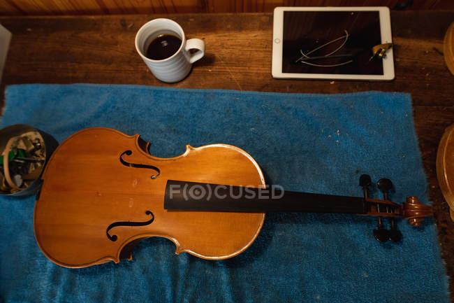 Ansicht einer Geige auf blauem Tuch in einer Geigenbauerwerkstatt mit Kaffeetasse und Tablet-Computer — Stockfoto