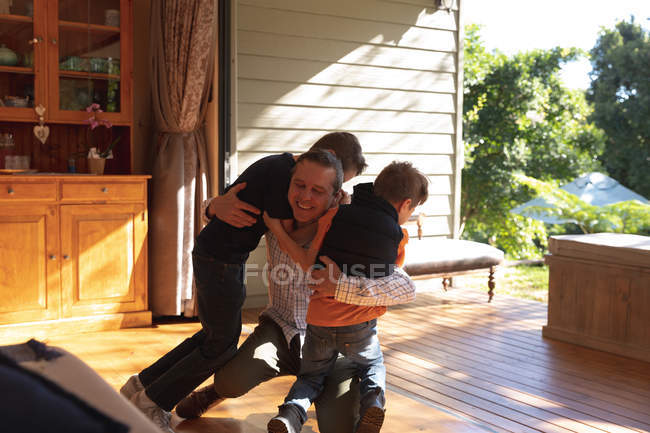 Вид спереди на белого мужчину средних лет, обнимающегося с двумя сыновьями-подростками после возвращения домой — стоковое фото