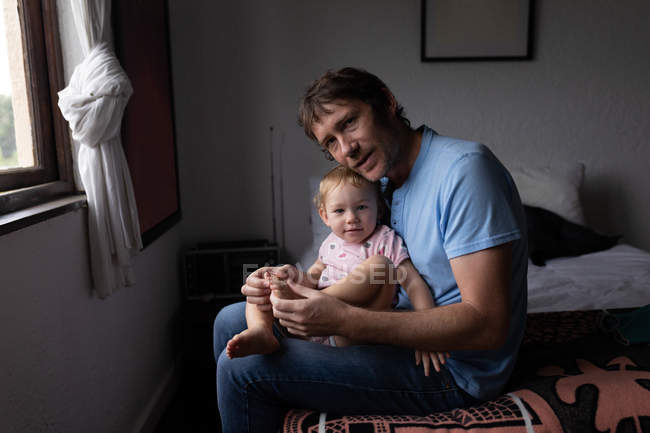 Retrato de um jovem pai caucasiano segurando seu bebê, sentado em uma cama — Fotografia de Stock