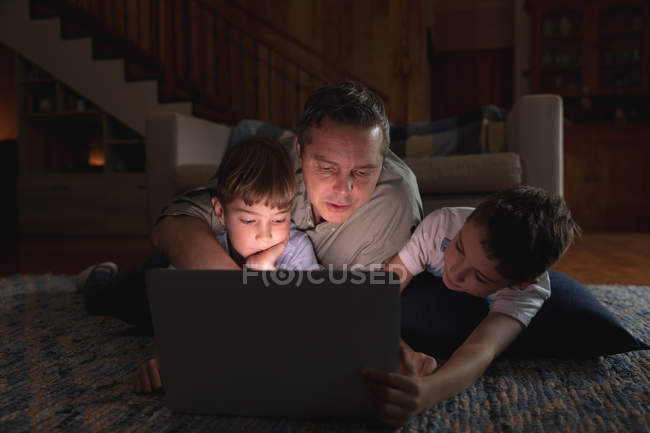 Frontansicht eines kaukasischen Mannes mittleren Alters und seiner vorpubertären Söhne mit einem Laptop im Wohnzimmer — Stockfoto