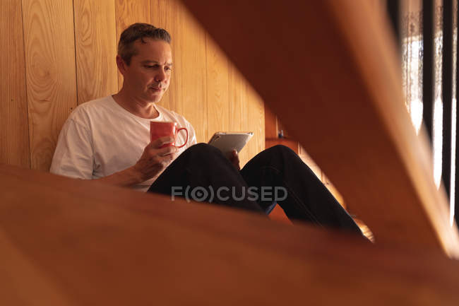 Seitenansicht eines kaukasischen Mannes mittleren Alters, der zu Hause auf einer Treppe sitzt und einen Tablet-Computer benutzt — Stockfoto
