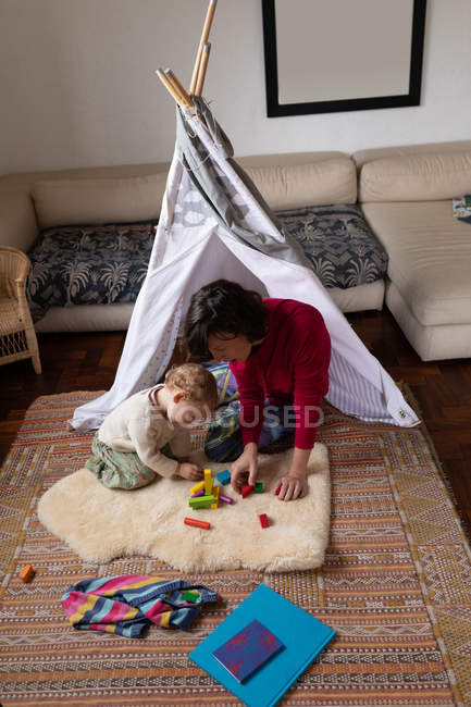 Передній вигляд, як молода кавказька мати бавиться з дитиною на підлозі, з наметом на задньому плані. — стокове фото