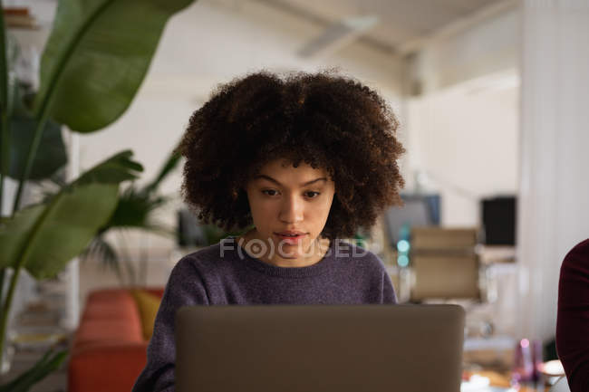 Передній план крупним планом молода змішана жінка, що сидить за столом, використовуючи ноутбук у творчому офісі — стокове фото