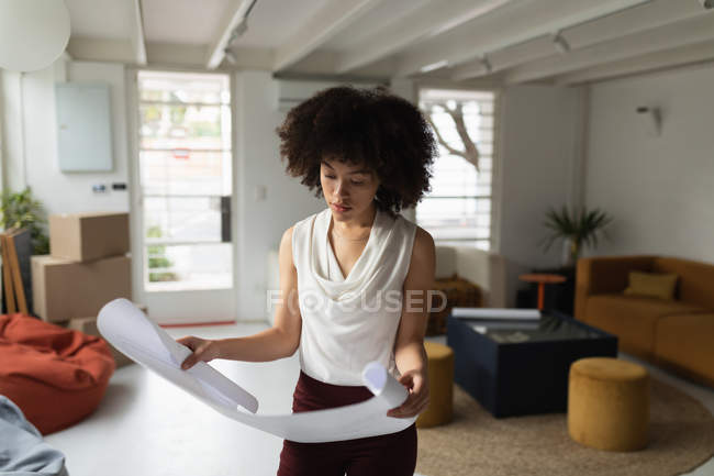Вид спереду крупним планом молода змішана жінка, що стоїть і перевіряє архітектурний малюнок в творчому офісі — стокове фото