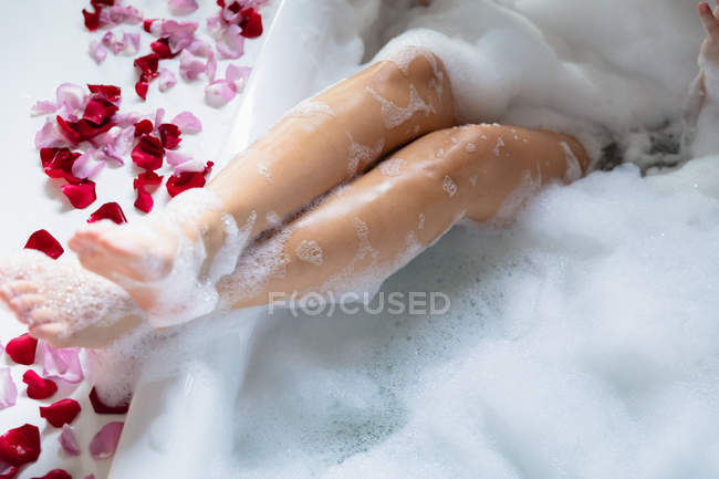 Nahaufnahme der Beine einer Frau, die am Rand mit Rosenblättern an der Seite angehoben wurde, während sie in einem Schaumbad liegt — Stockfoto