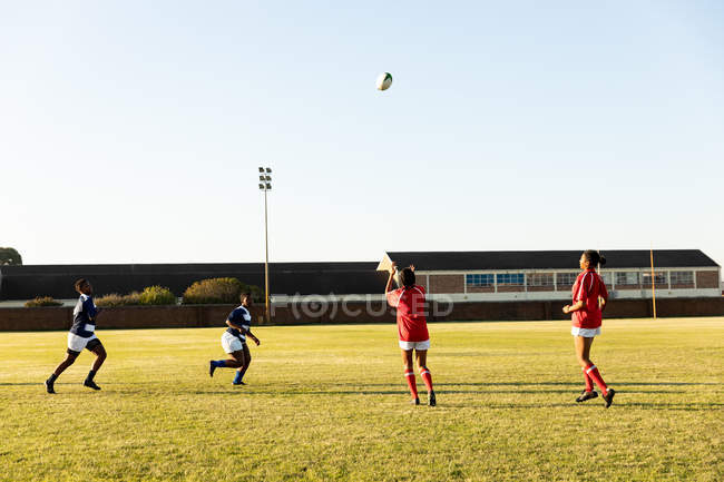 Vista laterale di un gruppo di giovani giocatrici di rugby multietniche, con la palla alta in aria durante una partita di rugby — Foto stock