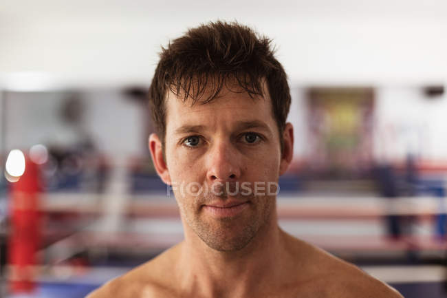 Porträt eines jungen kaukasischen Boxers in einer Boxhalle, der in die Kamera blickt — Stockfoto