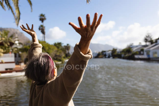 Rear view of a senior Caucasian woman with arms in the air by a lake — Stock Photo