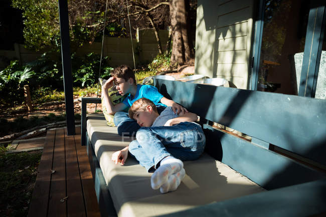 Vista lateral de dos niños caucásicos pre adolescentes acostados en un banco en un jardín - foto de stock