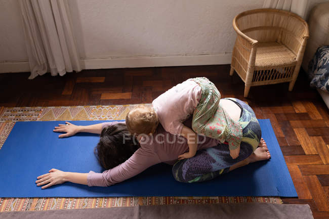 Вид сбоку на молодую кавказскую мать в позе йоги с ребенком наверху — стоковое фото