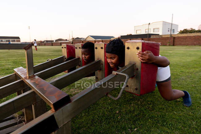 Frontansicht von zwei jungen erwachsenen afrikanisch-amerikanischen Rugbyspielerinnen, die während einer Teamtrainingseinheit eine Gedrängemaschine auf einem Rugbyfeld benutzen — Stockfoto