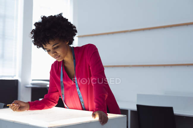 Front view close up of a young mixed race female fashion student working on a design drawing on a lightbox in a studio at fashion college — Stock Photo