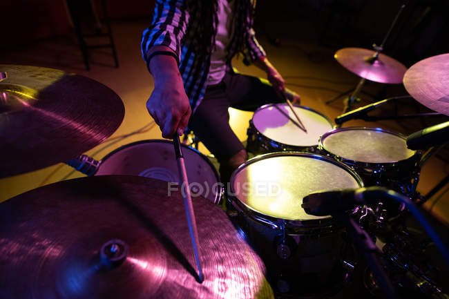 Vista frontal sección central del baterista masculino tocando un kit de batería durante una sesión en un estudio de grabación - foto de stock