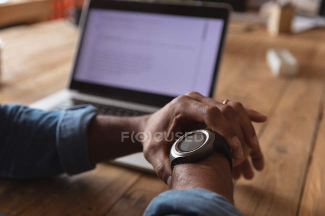 Close up of the hands of man sitting at a desk checking his watch and working on a laptop computer in a creative office — Stock Photo
