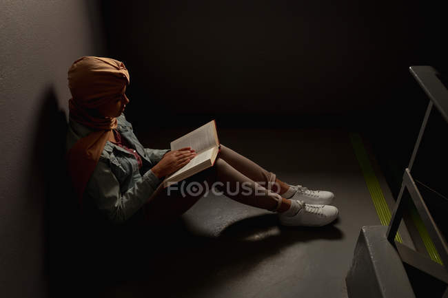 Side view of a young Asian female student wearing a hijab reading a book on a staircase — Stock Photo