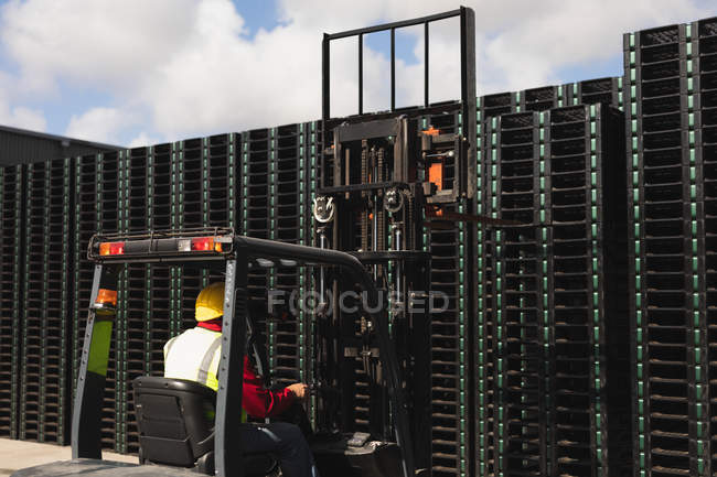 Rear view close up of a middle aged Caucasian male factory worker using a forklift truck to move a stack of pallets outside a warehouse at a factory — Stock Photo