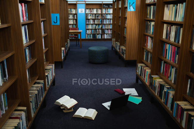 Interior of a library with rows of bookshelves, a seat and books and a laptop computer on a floor — Stock Photo