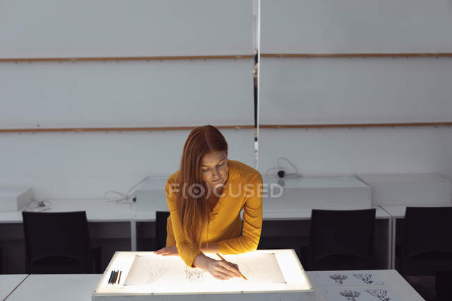 Frontansicht einer jungen kaukasischen Modestudentin, die in einem Atelier der Modehochschule an einer Designzeichnung auf einem Leuchtkasten arbeitet — Stockfoto