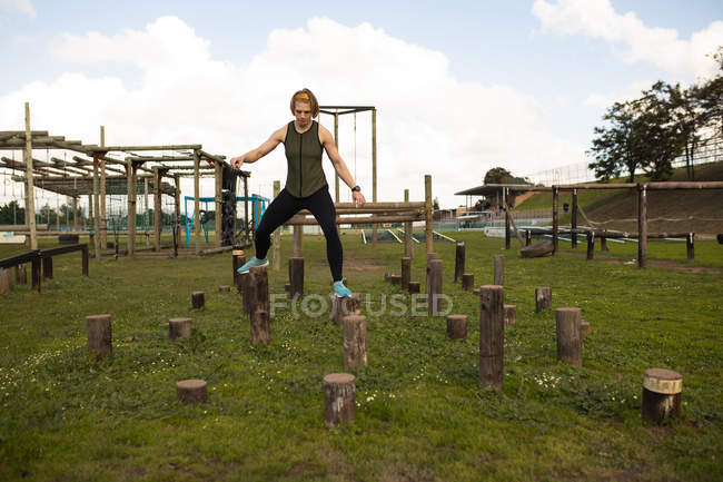 Vue de face d'une jeune femme caucasienne sautant entre des poteaux en bois dans une salle de gym extérieure lors d'une séance d'entraînement de bootcamp — Photo de stock