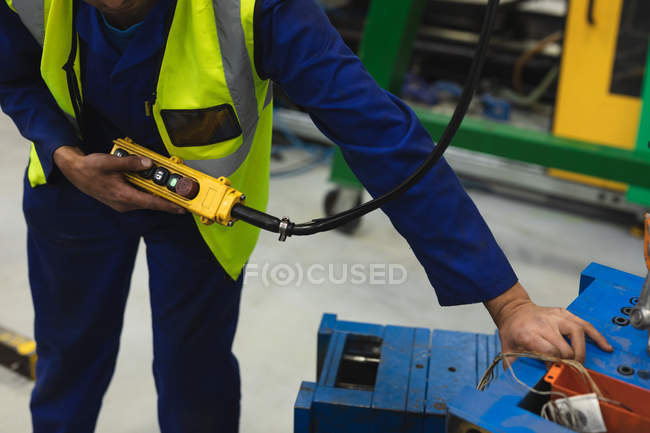 Side view mid section of a middle aged mixed race male factory worker moving machine parts on a trolley and operating a lifting chain in a loading area in a warehouse at a processing plant — Stock Photo