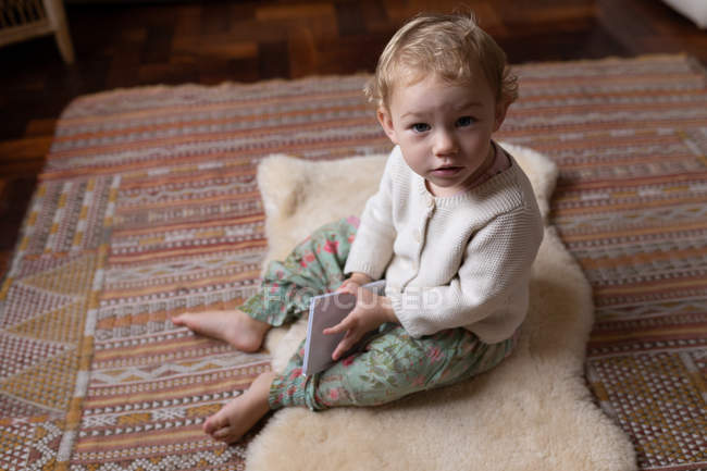 Porträt eines kaukasischen Babys, das barfuß auf dem Boden sitzt und ein Notizbuch in der Hand hält — Stockfoto