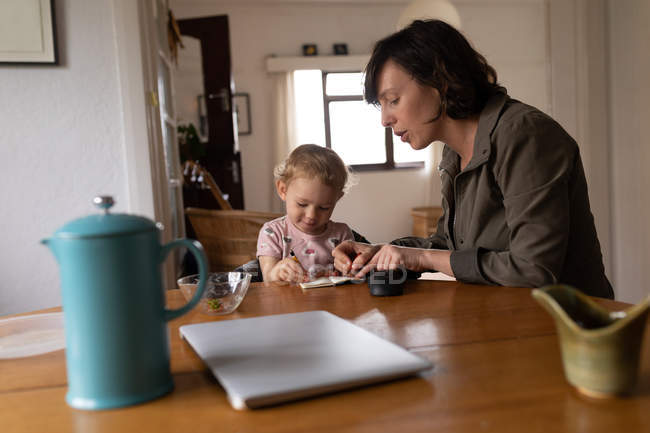 Side view of a young Caucasian mother coloring with her baby, sitting at a table — Stock Photo