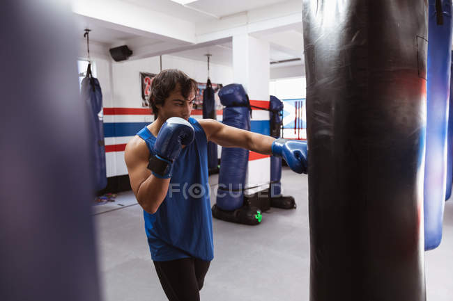 Vue de côté gros plan d'un jeune boxeur masculin de race mixte dans un gymnase de boxe frappant un punchbag — Photo de stock
