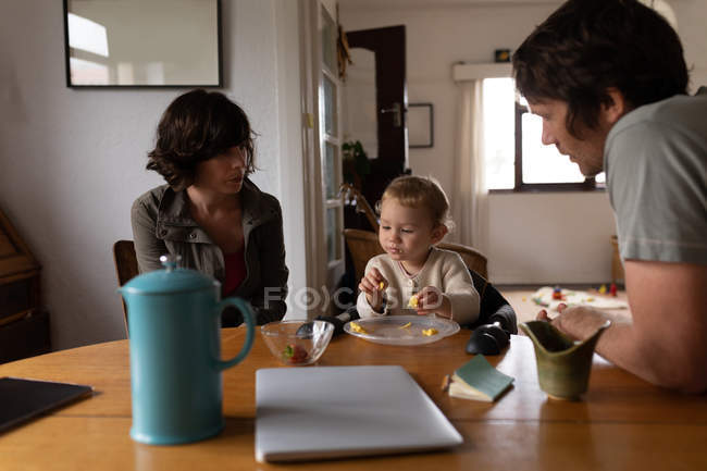 Vista lateral de jovens pais caucasianos sentados a uma mesa e comendo bebê — Fotografia de Stock