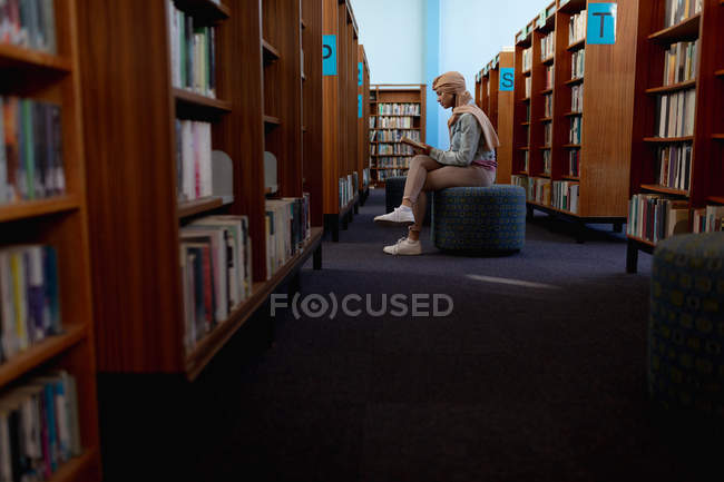 Vista lateral de perto de uma jovem estudante asiática vestindo um hijab lendo um livro e estudando em uma biblioteca — Fotografia de Stock
